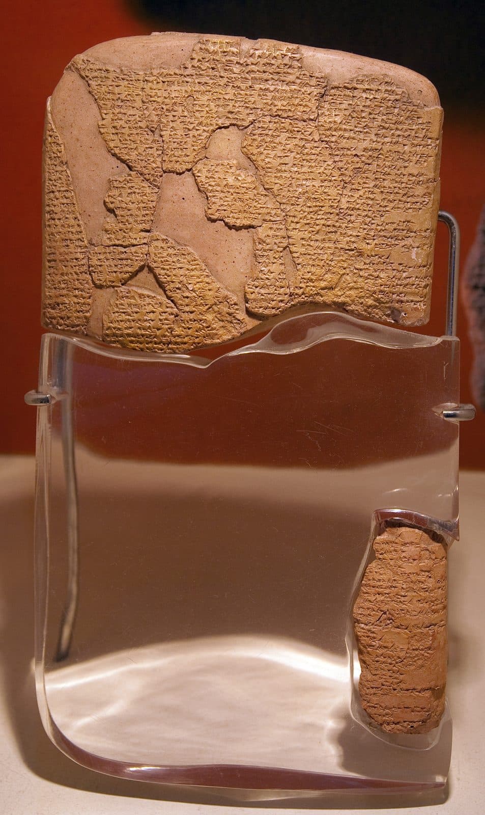 A broken clay tablet covered in cuneiform, set in a clear stand.