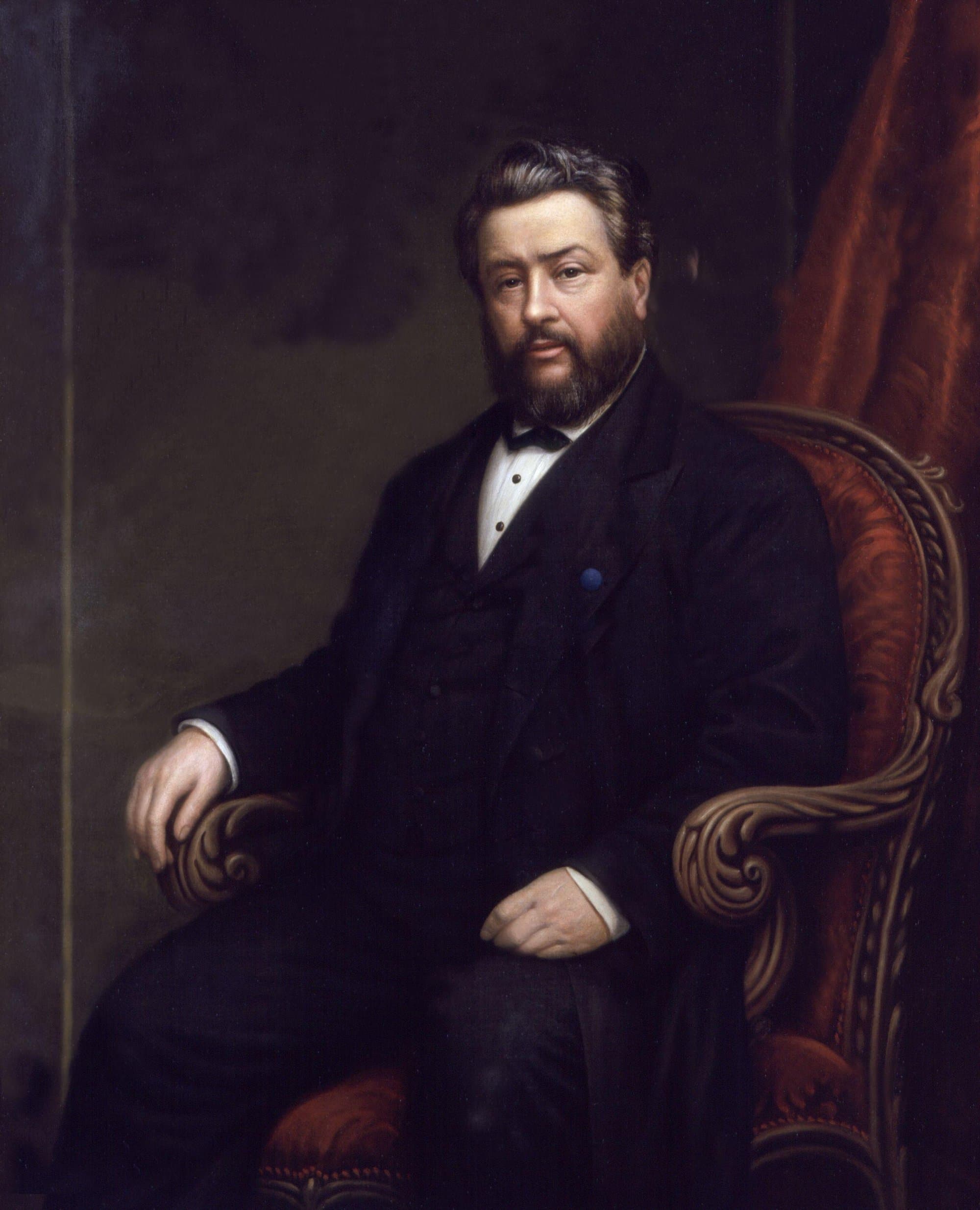 A painted portrait of a heavily built bearded man in a black suit and bow tie, seated in a carved armchair with red upholstery, one hand on the chair's arm and a red curtain behind him.
