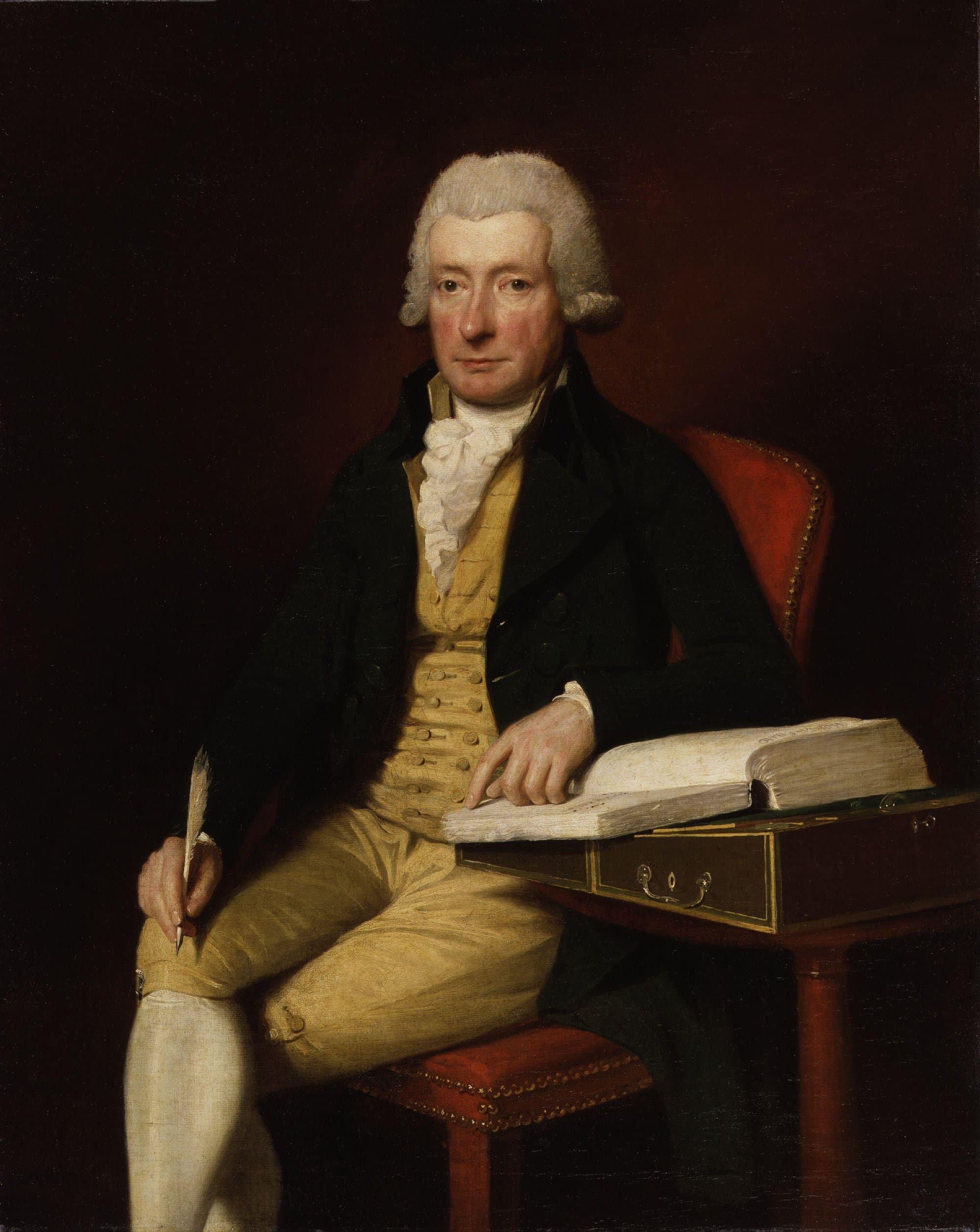 A painted portrait of a man in a grey powdered wig, dark coat and yellow waistcoat and breeches, seated beside a writing desk with a quill in one hand and the other resting on an open book.