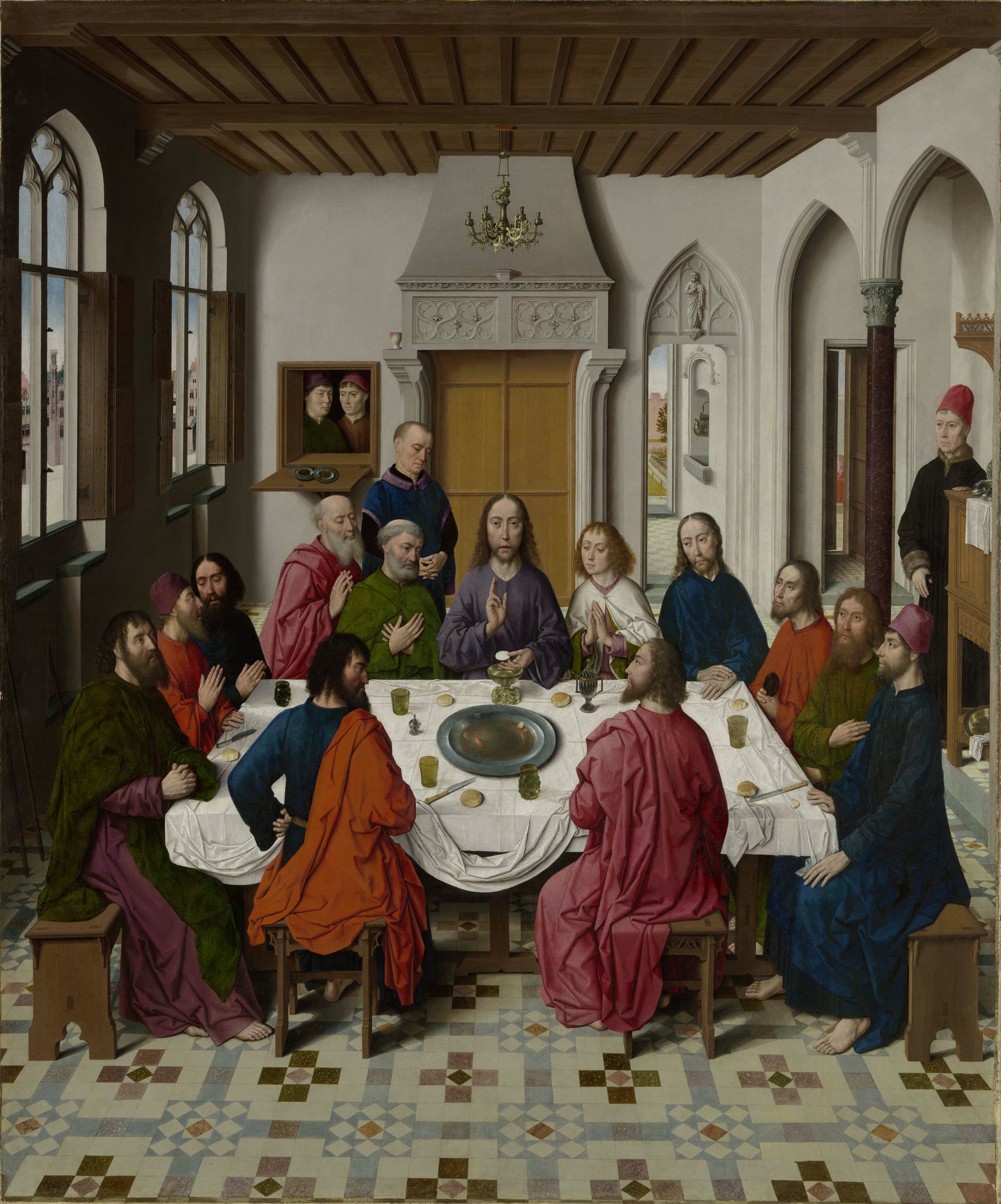 Jesus sits at the centre of a white-covered table in a vaulted Flemish room, raising His hand in blessing over a wafer and a cup, with the twelve disciples seated around Him and servants standing at the sides.