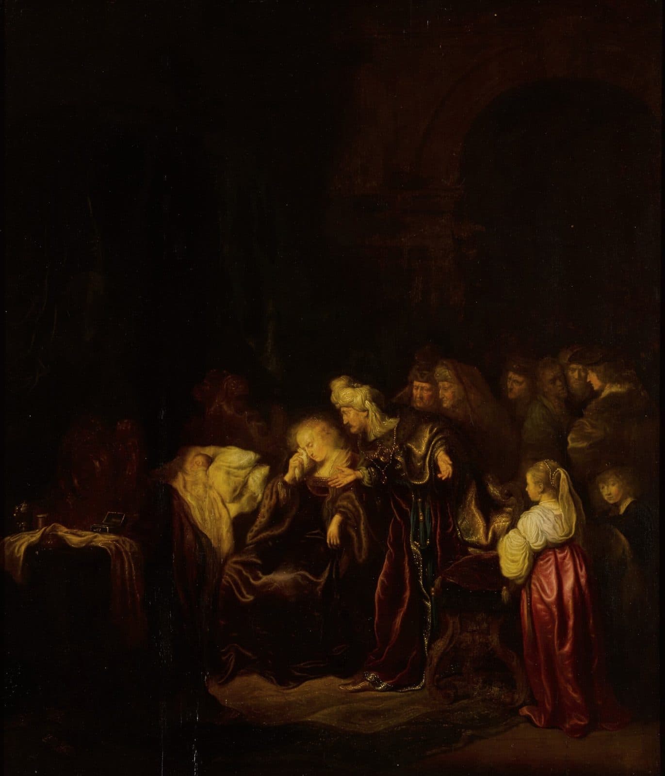 A dark painting of a dead infant lying on a bed under a pale cloth, a fair-haired woman beside it wiping her eyes with a handkerchief, a turbaned man in a rich robe bending toward her with an open hand, and courtiers and a girl in a red skirt looking on.