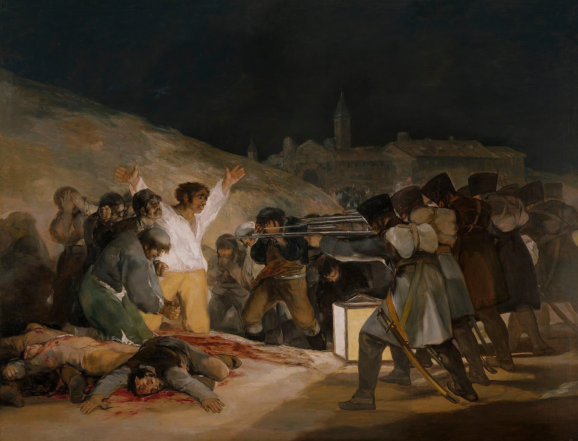 At night a line of soldiers aims rifles at a group of unarmed men. One man in a white shirt raises his arms wide in the lantern light, and bodies lie on the ground before him.
