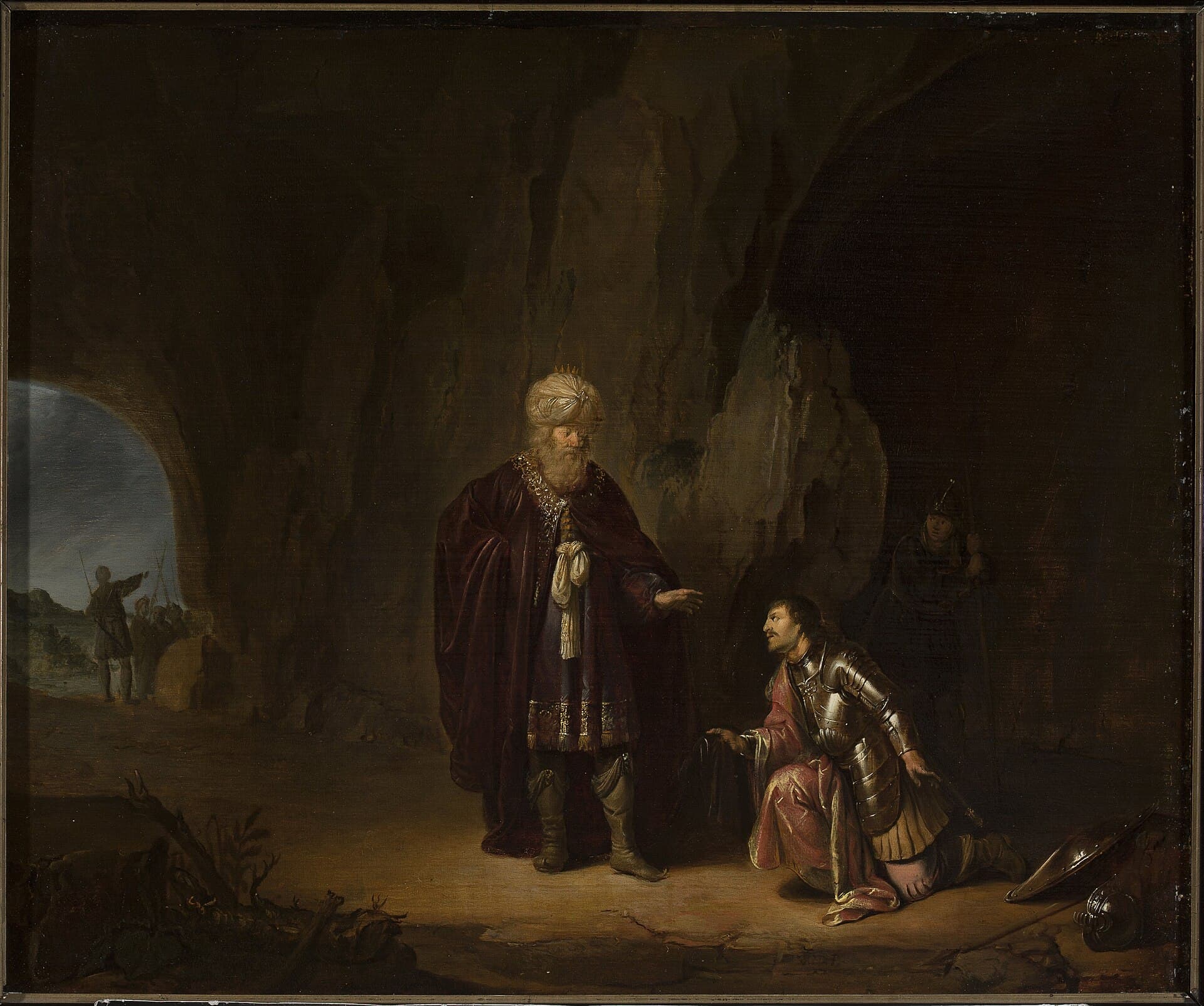 Inside a dark cave, an old king in a crowned turban and a long purple robe looks down at a younger man in armor who kneels before him holding a piece of cloth, with a helmet and shield on the ground, a guard in the shadows and soldiers at the sunlit mouth of the cave.