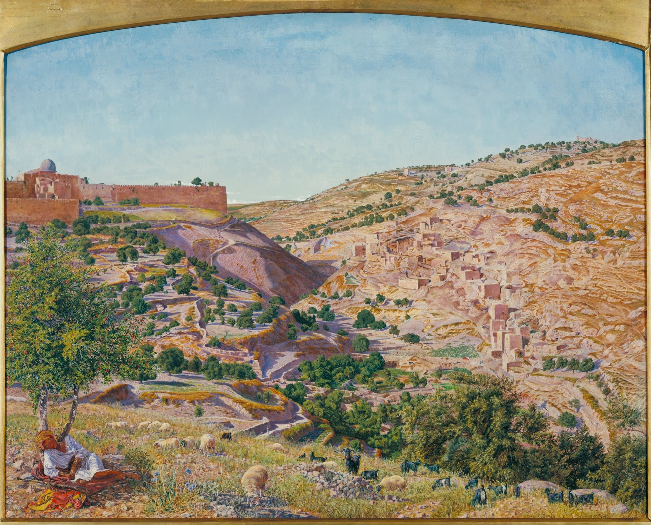 A sunlit valley seen from a hillside to the south. City walls with a grey dome stand on the left above a bare ridge, a village of flat-roofed houses climbs the slope on the right, and a shepherd rests under a tree with sheep and goats in the foreground.