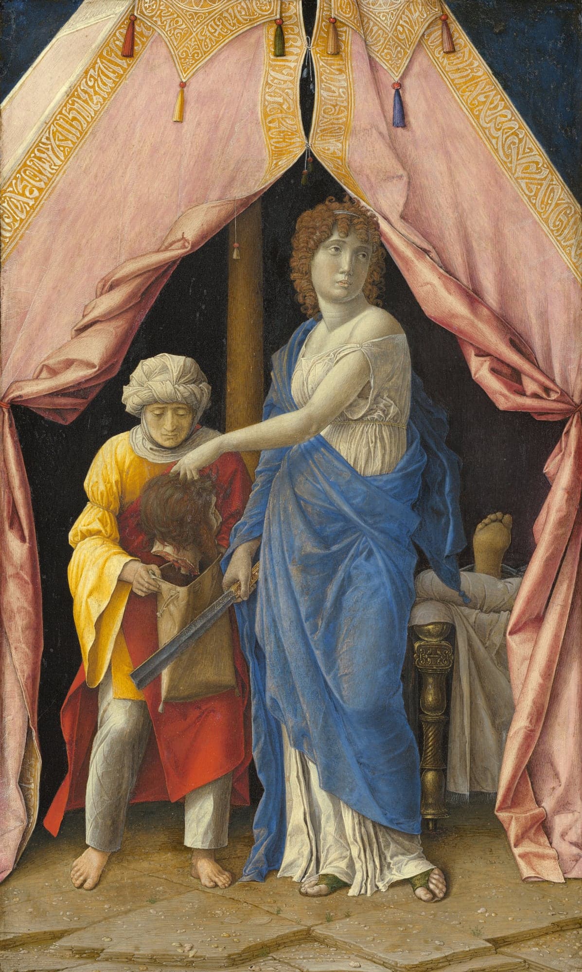 Inside a pink tent hung with gold-lettered borders, a young woman in a blue cloak over a white gown lowers a severed head into a sack held open by an older maid in a yellow and red robe, a sword hanging from her other hand, while a bare foot shows on the bed behind them.
