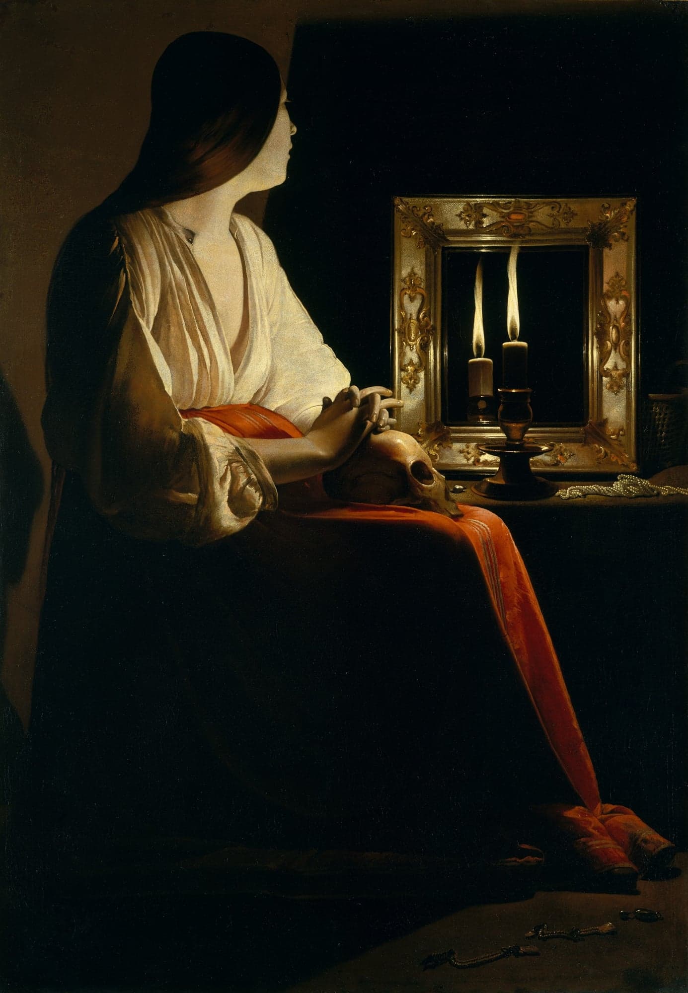 A painting of a woman in a white blouse and a red skirt seated in the dark, her hands folded on a skull in her lap. She looks toward a mirror in a gilded frame, where a candle on the table is doubled, and a string of pearls lies beside it with more jewels scattered at her feet.