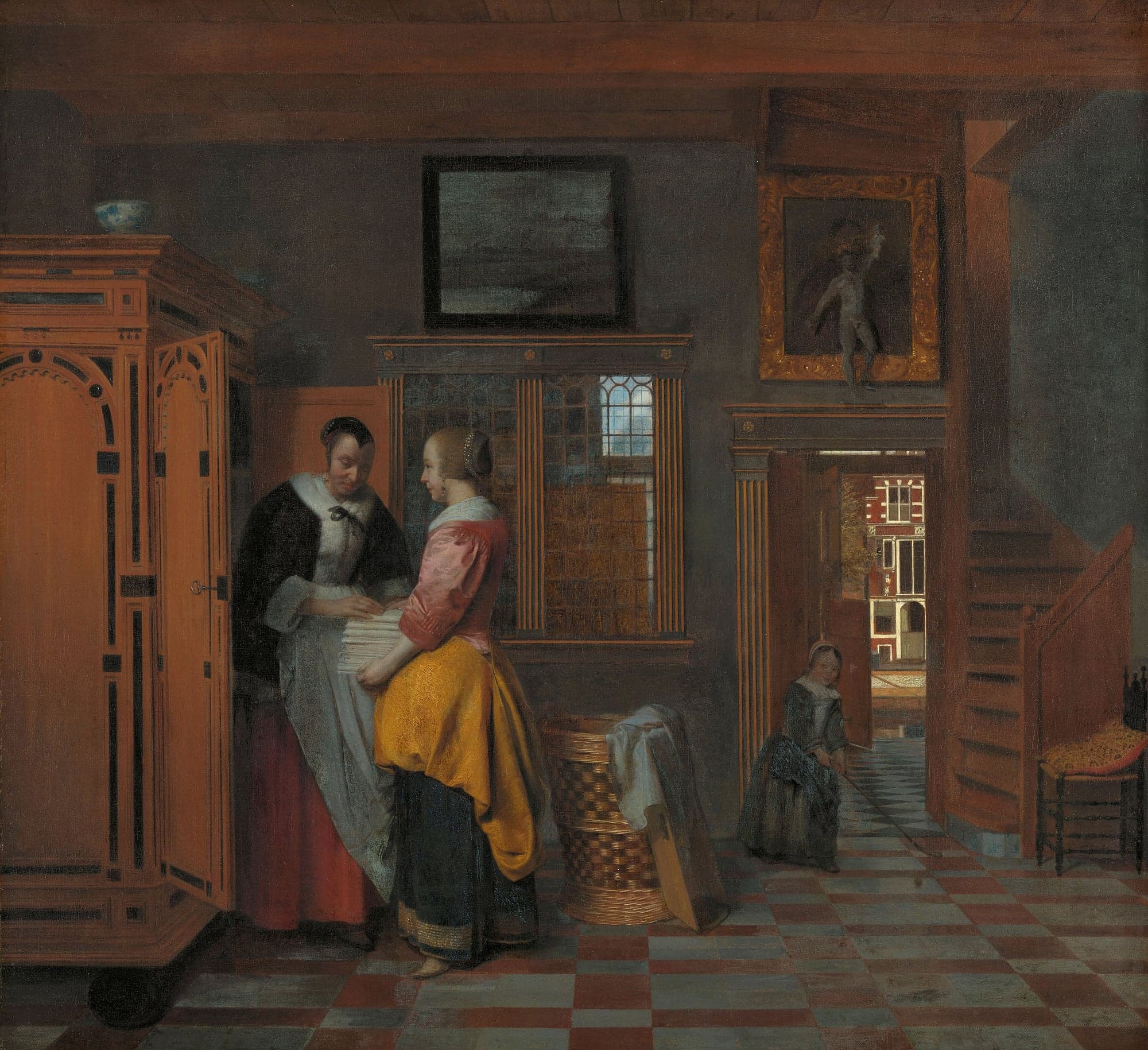 A painting of a Dutch room with a checkered floor, where two women stand at a tall open cupboard and pass a stack of folded linen between them. A child plays with a stick by an open door that looks out on a canal street.