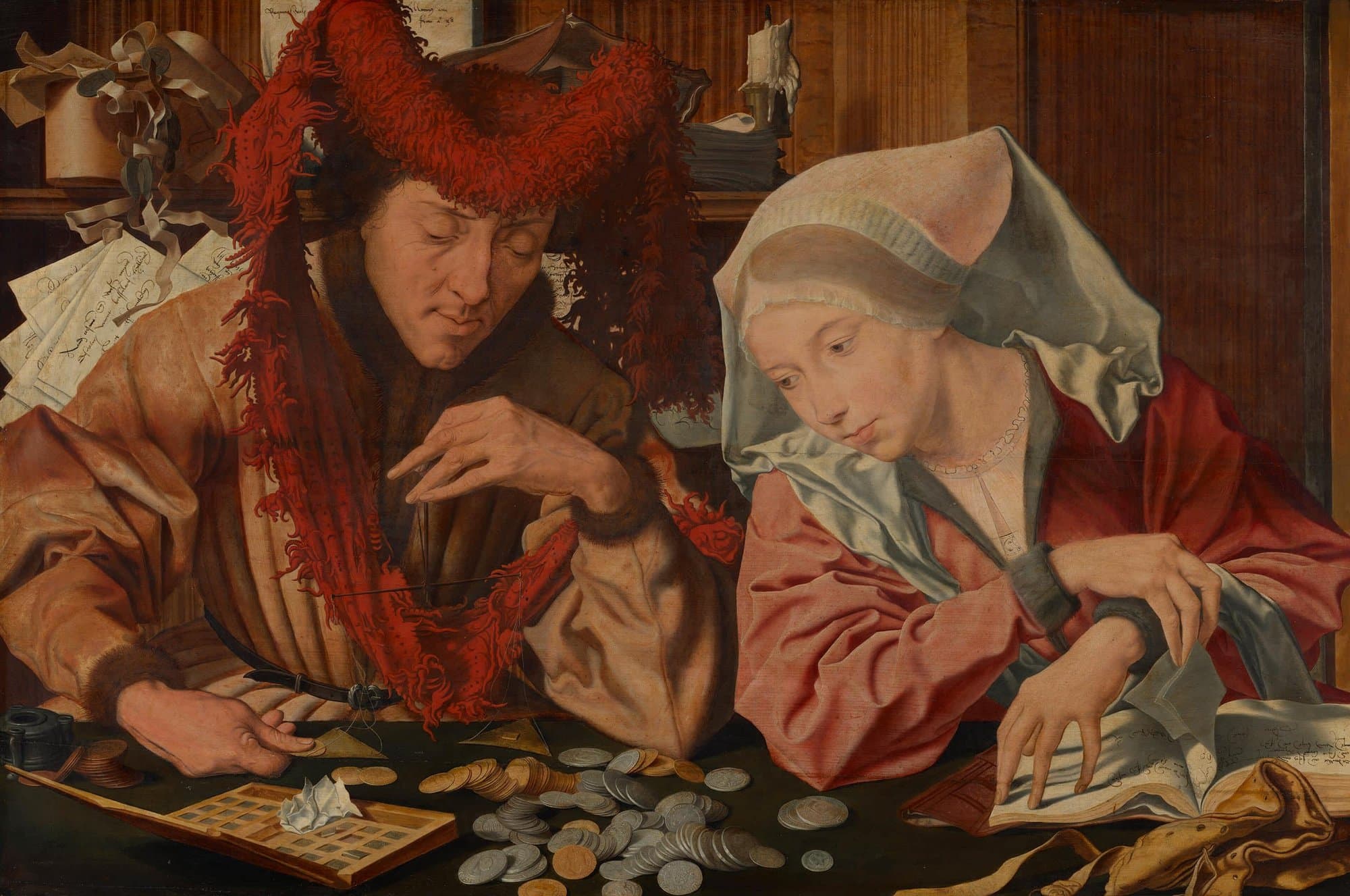 A man in a great red fur hat weighs a coin on a small balance over a table strewn with silver and gold coins and an open box of weights, while his wife in a white headdress and red gown leans beside him, her hand on the page of an open account book. Papers, a candle and a box crowd the shelf behind them.