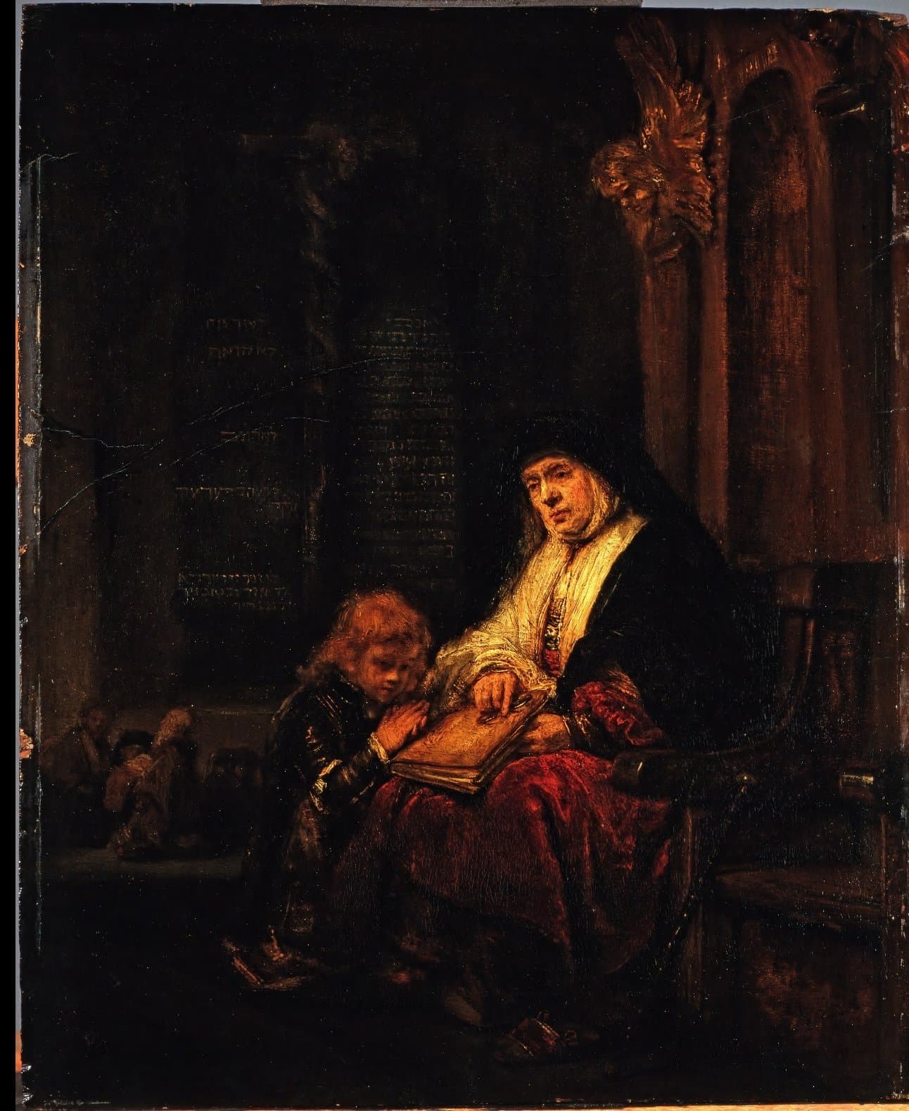 A dark painting of a temple interior: an old woman in a black hood and a white shawl sits in a carved chair with a large book open on her lap and points to its page, while a fair-haired boy kneels against her knee with his hands clasped, and behind them stand tablets lettered in Hebrew and a carved winged figure on a column.