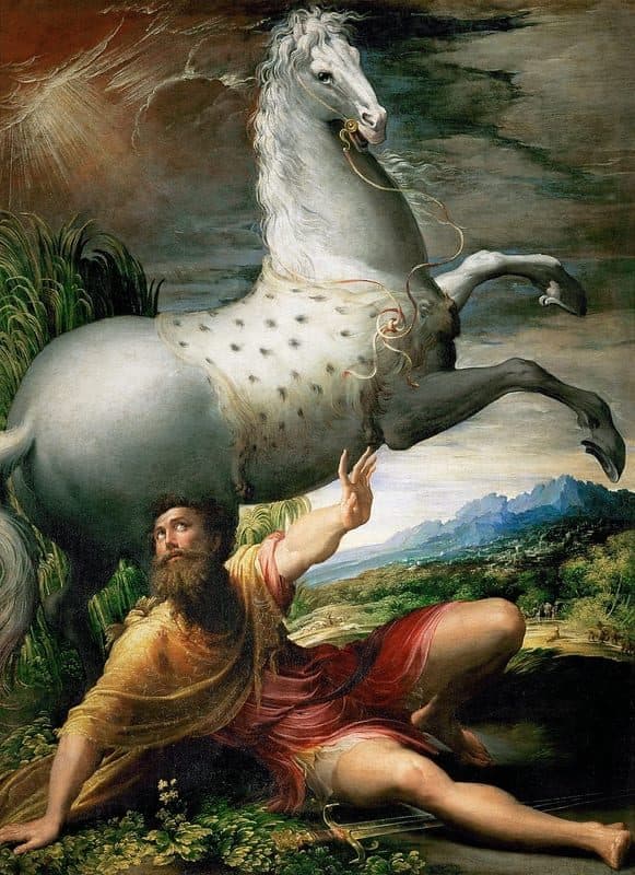 A bearded man in a yellow cloak and a red robe lies on the ground with one arm raised toward rays of light in the sky, while a white dappled horse rears above him