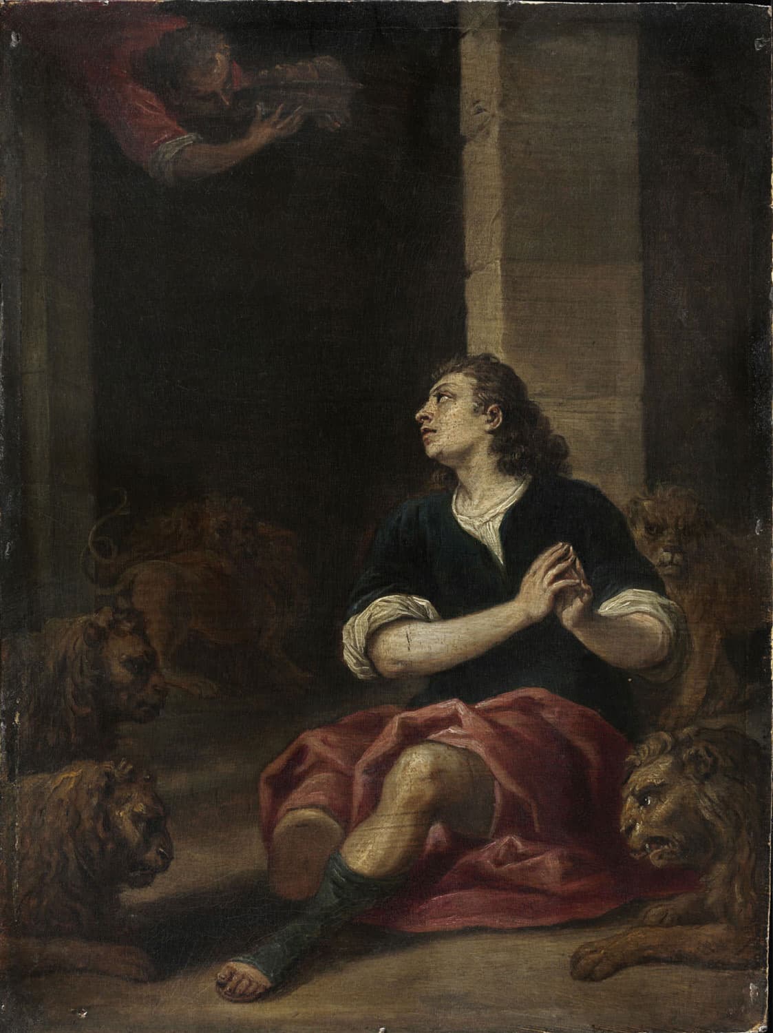 A painting of a man in a dark jacket and a red cloth seated on the floor of a stone pit with his hands joined, looking up at a figure in red who leans over the edge above, while lions lie and prowl around him.