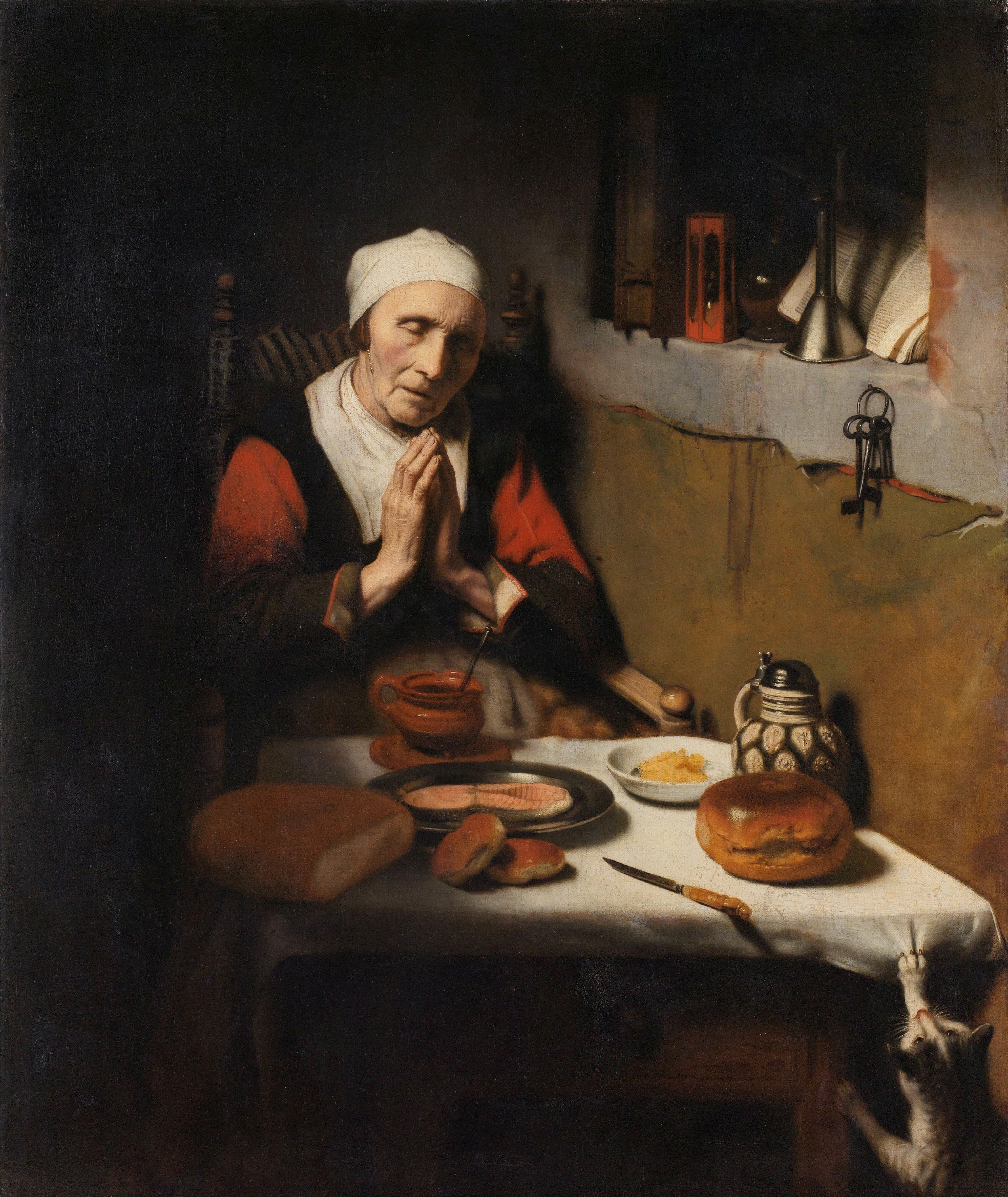 An old woman in a white cap sits at a table laid with bread, fish, butter and a stoneware jug, her eyes closed and her hands pressed together, while a cat below the table pulls at the cloth and keys hang on the wall behind her.
