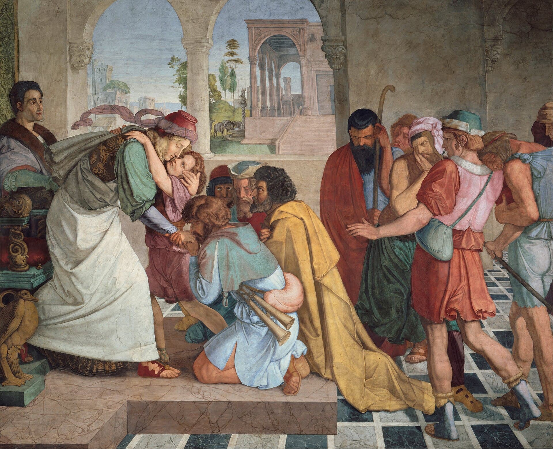 Joseph, in a white robe, bends to embrace his youngest brother while a kneeling brother kisses his hand; the other brothers kneel or stand around them, some covering their faces, in a hall of arches that opens onto a city.
