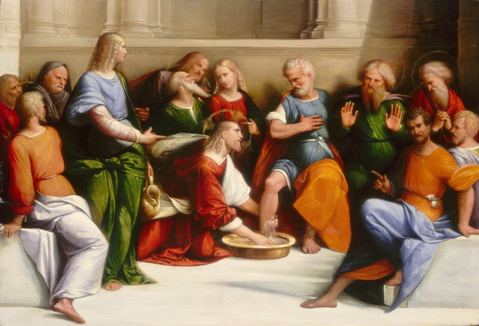 Jesus kneels on a stone floor in a red robe and washes the foot of an old apostle seated above Him, while the other apostles watch from a bench under a classical portico.