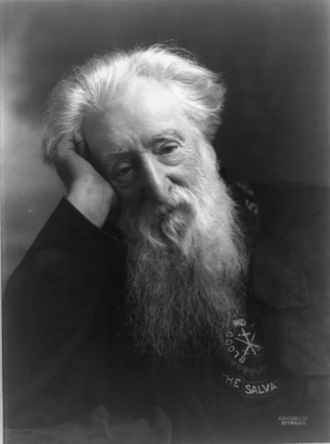 A black and white photograph of an old man with long white hair and a long white beard, his head resting on his raised right hand, wearing a dark uniform with an embroidered crest and the words The Salvation Army on the collar.