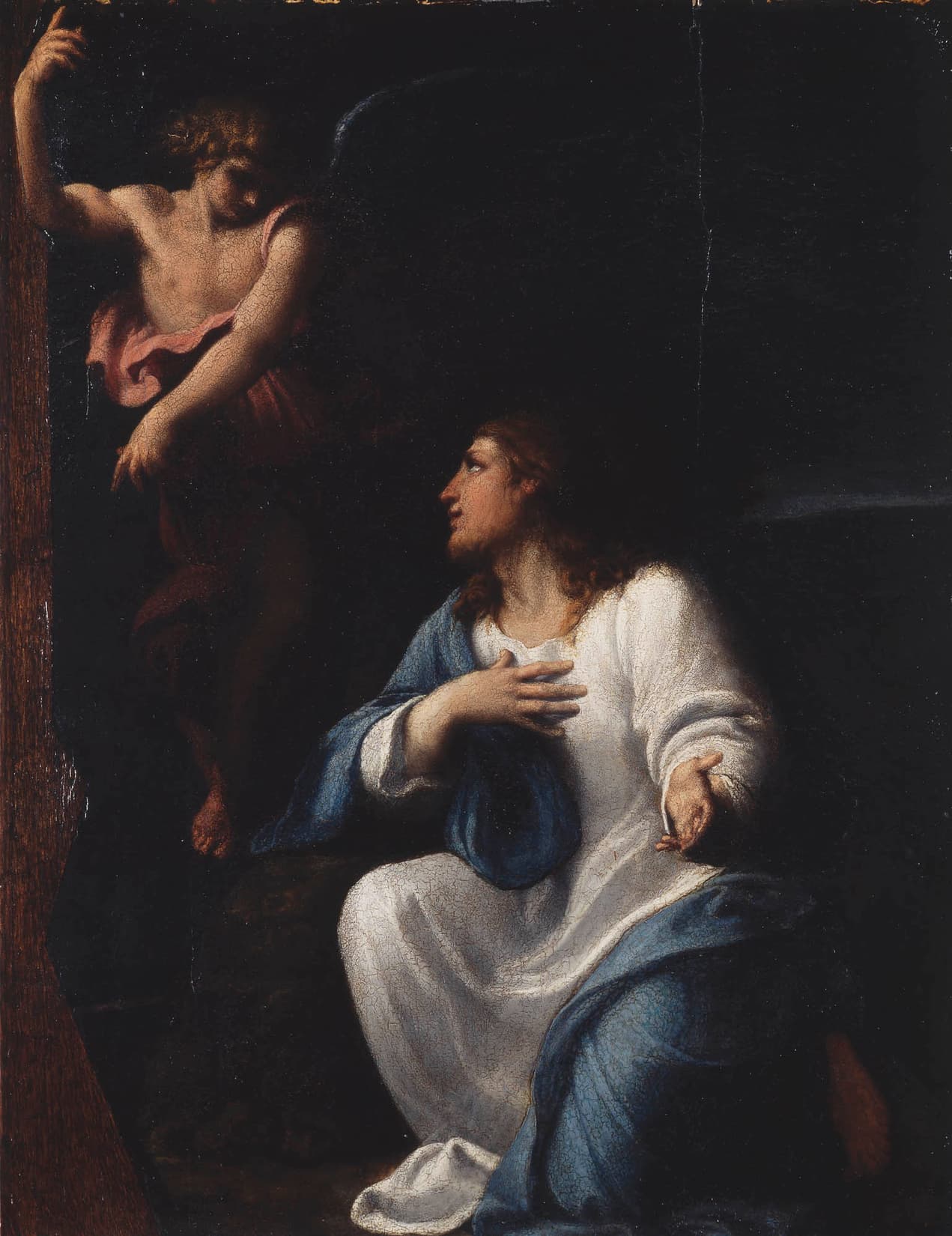 Christ kneels in a white robe and a blue mantle with one hand on His chest and looks up at an angel who comes down out of the dark above Him, pointing upward.