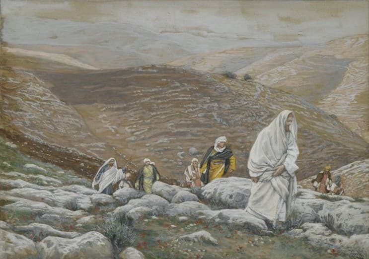 A man in a white mantle climbs a rocky hillside in the foreground, and a line of travellers in robes and head cloths follows him up the slope below bare brown hills.