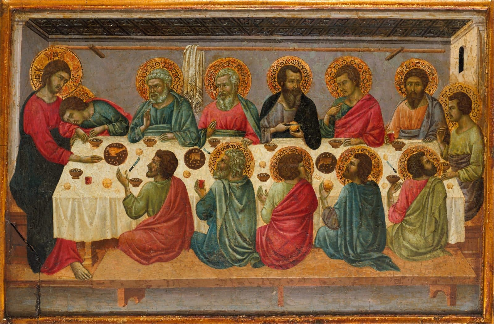 Jesus stands at the left end of a long table with a young disciple asleep against Him; six apostles sit behind the table and five kneel before it