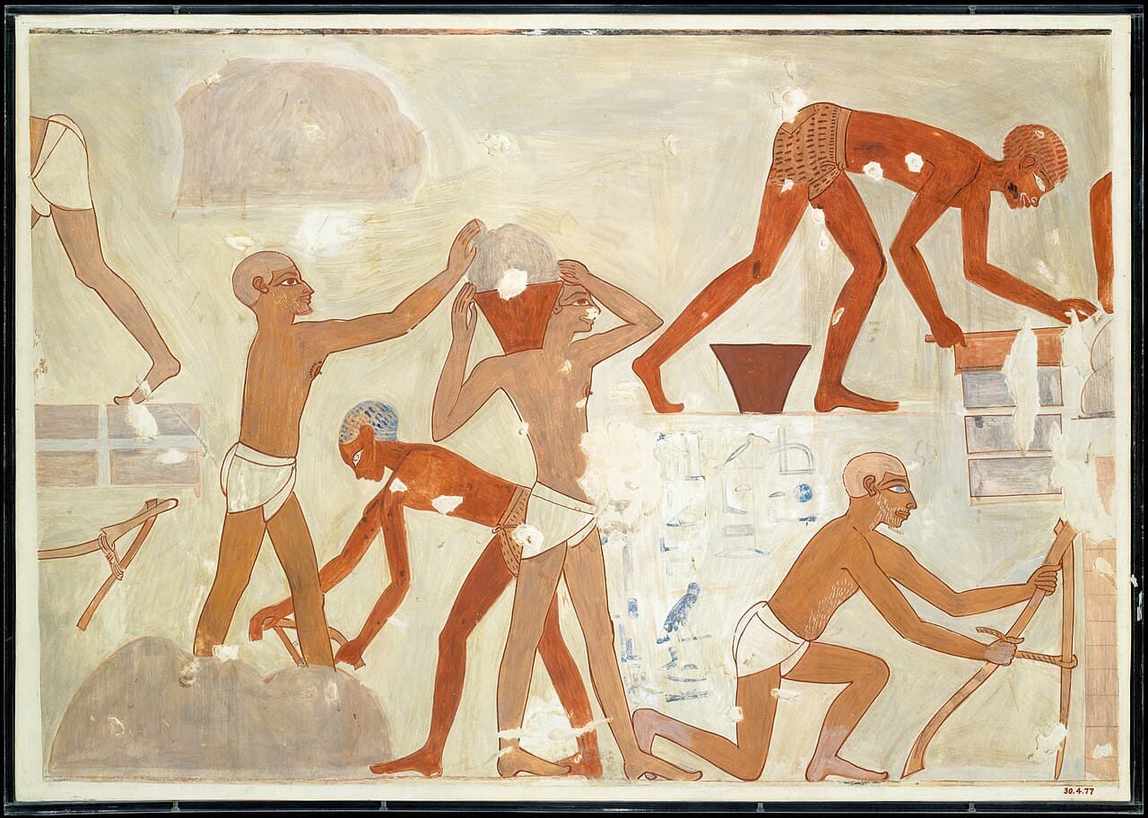 An Egyptian wall painting of brickmakers at work: one man hoes wet clay, two carry clay in jars on their heads, one stoops to set bricks in rows, and one kneels with a tool beside a stack of bricks.