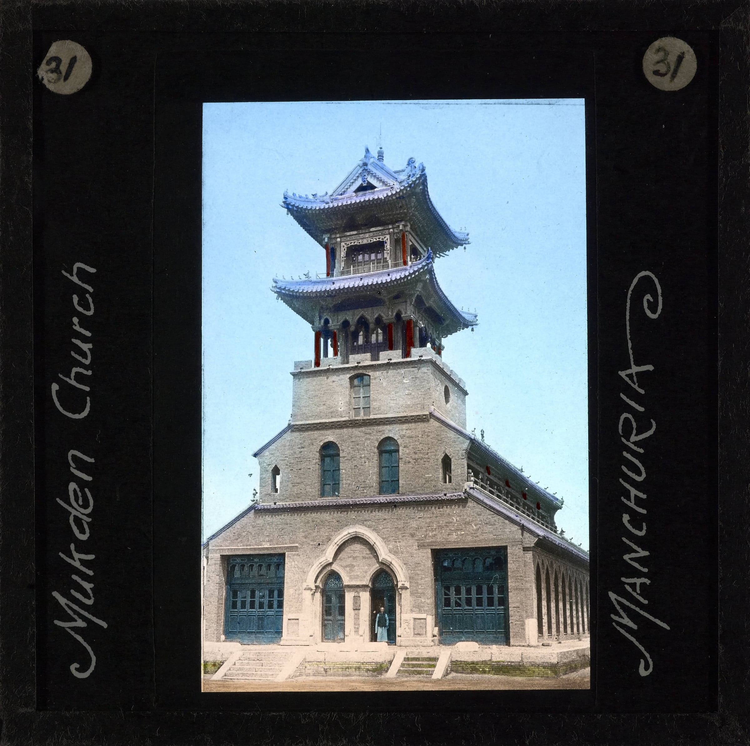 A hand-coloured lantern slide of a brick church with a tall tower in Chinese pagoda style, a small figure in its doorway, framed in black with the words Mukden Church and Manchuria.
