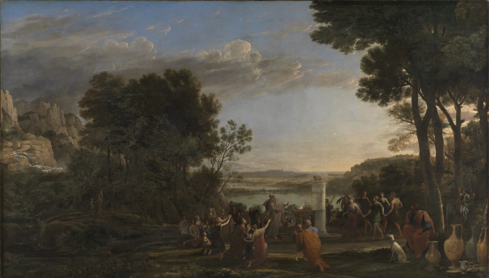 A wide wooded landscape at evening with a lake and hills behind. In the middle a small golden calf stands on a white column beside a smoking altar, a robed man raises his hand before it, people kneel with their arms lifted, and a ring of dancers circles the column. Two small figures come down a slope from the rocky heights at the left.