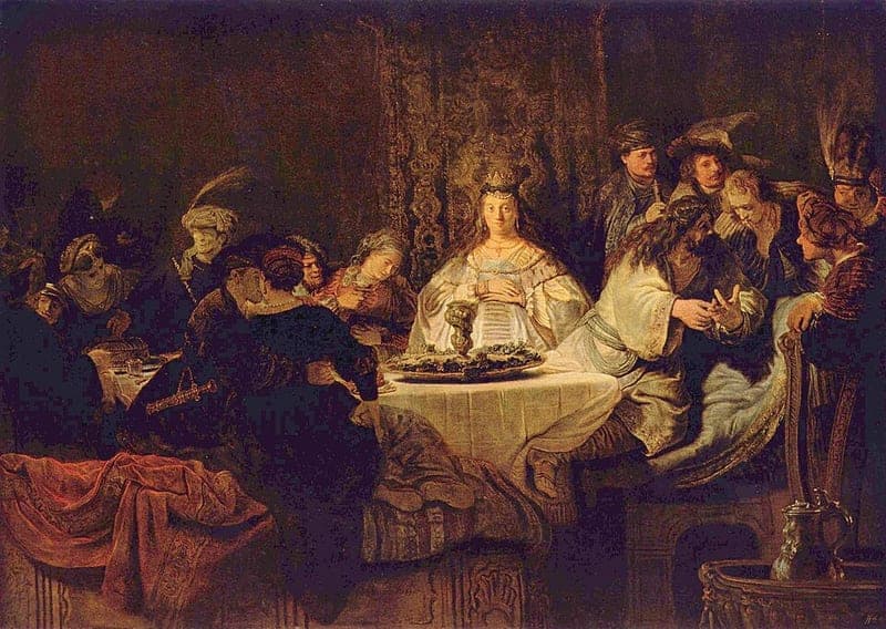 Rembrandt's painting of a wedding feast in a dark hall: a bride in a pale gown and a small crown sits upright behind a round table set with a cloth, a dish and a tall cup, a long-haired man in a pale robe leans back at the right and speaks with raised hands to men in turbans and plumed hats, and couples talk and embrace at the left