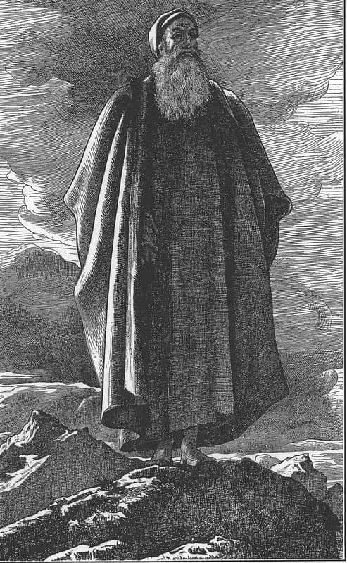 An engraving of an old man with a long white beard and a turban, wrapped in a heavy cloak that falls to his bare feet, standing alone on a rocky summit with mountain peaks and a clouded sky behind him.