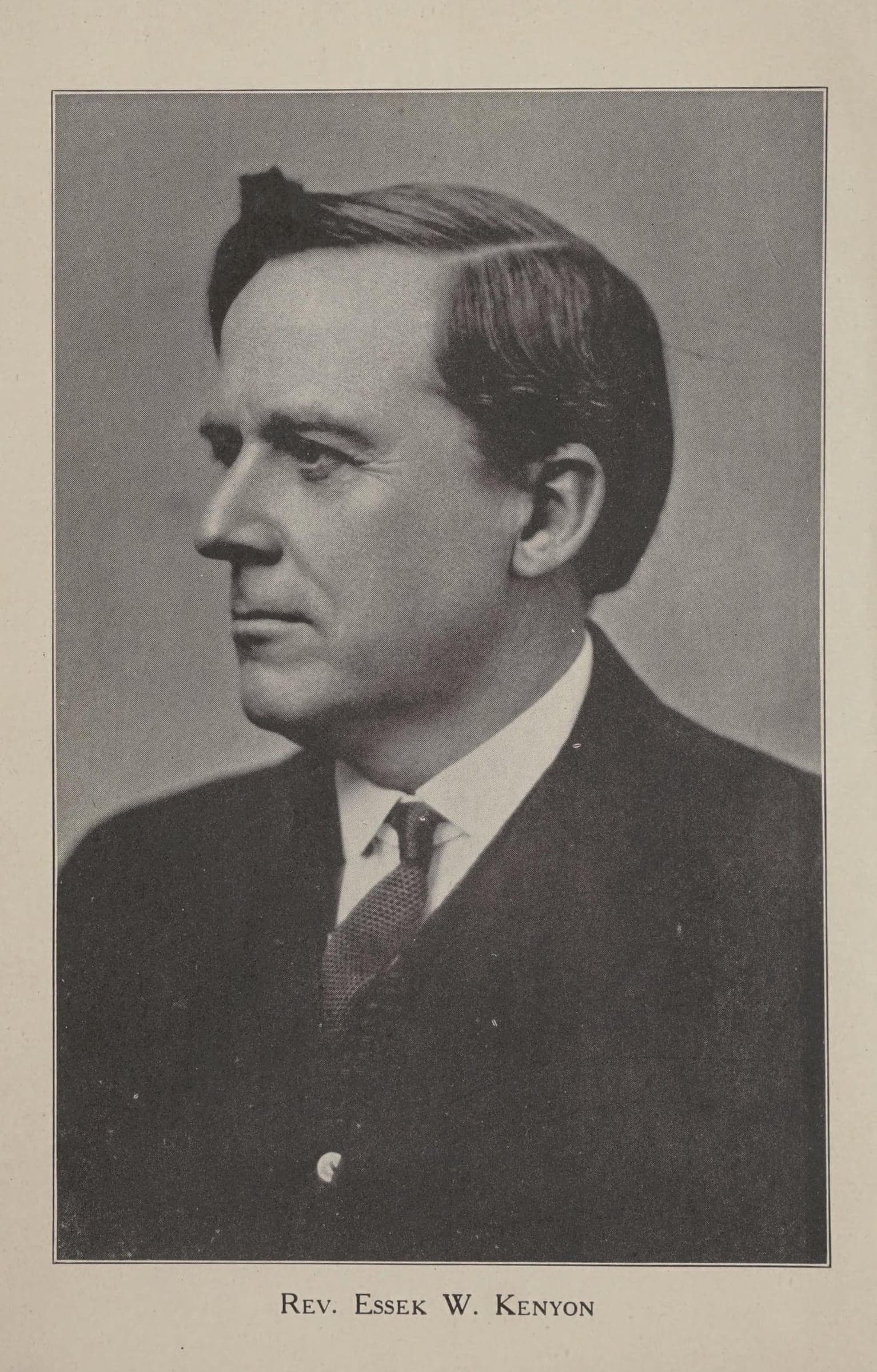 A photograph of a dark-haired man in a dark suit and tie, seen in profile facing left, printed on a book page above the caption Rev. Essek W. Kenyon.