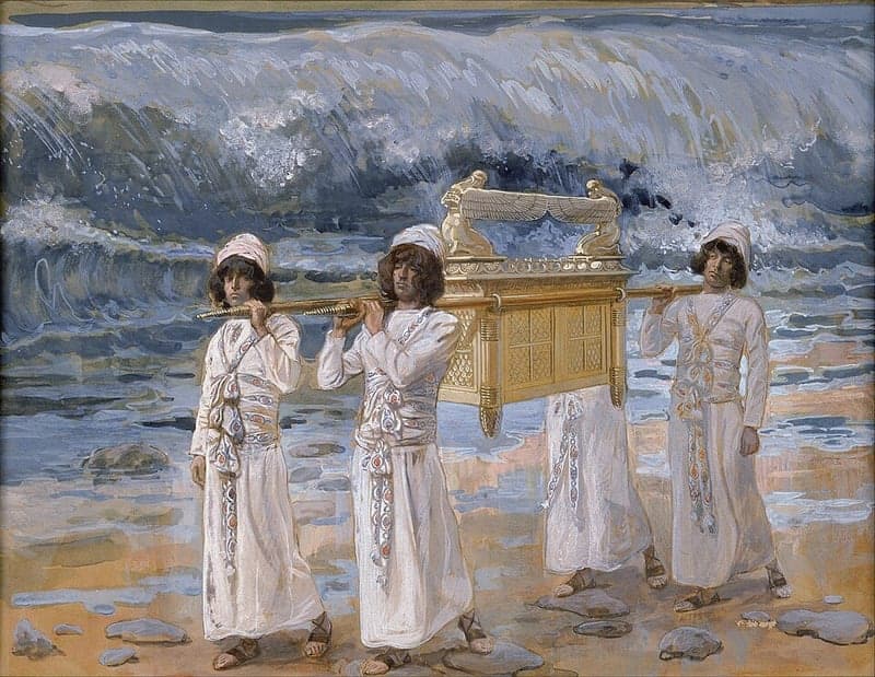 Four young priests in white robes and white head cloths carry the golden ark of the covenant on poles across a stony riverbed, while a towering wave of grey and white water stands behind them.