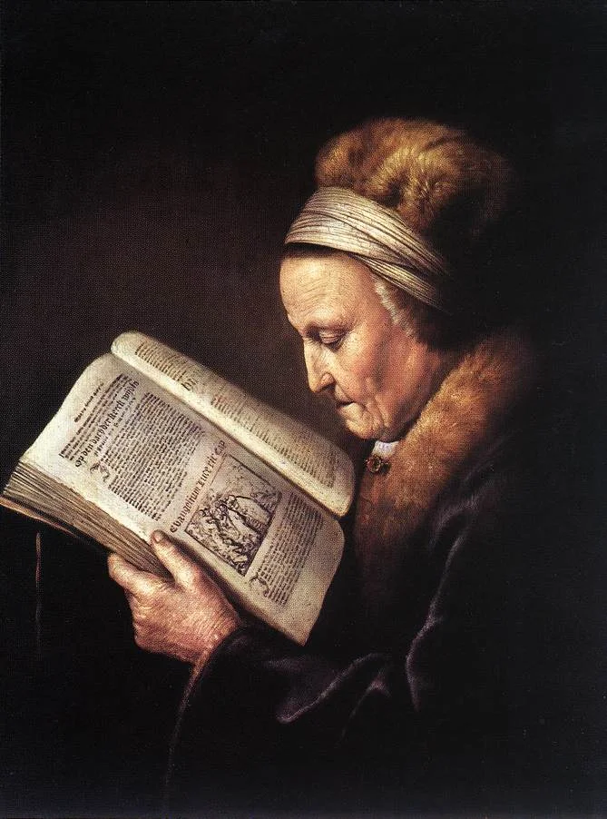 An old woman in a fur-trimmed cloak and a pale headband reads a large printed Bible held open in her hands against a dark ground.