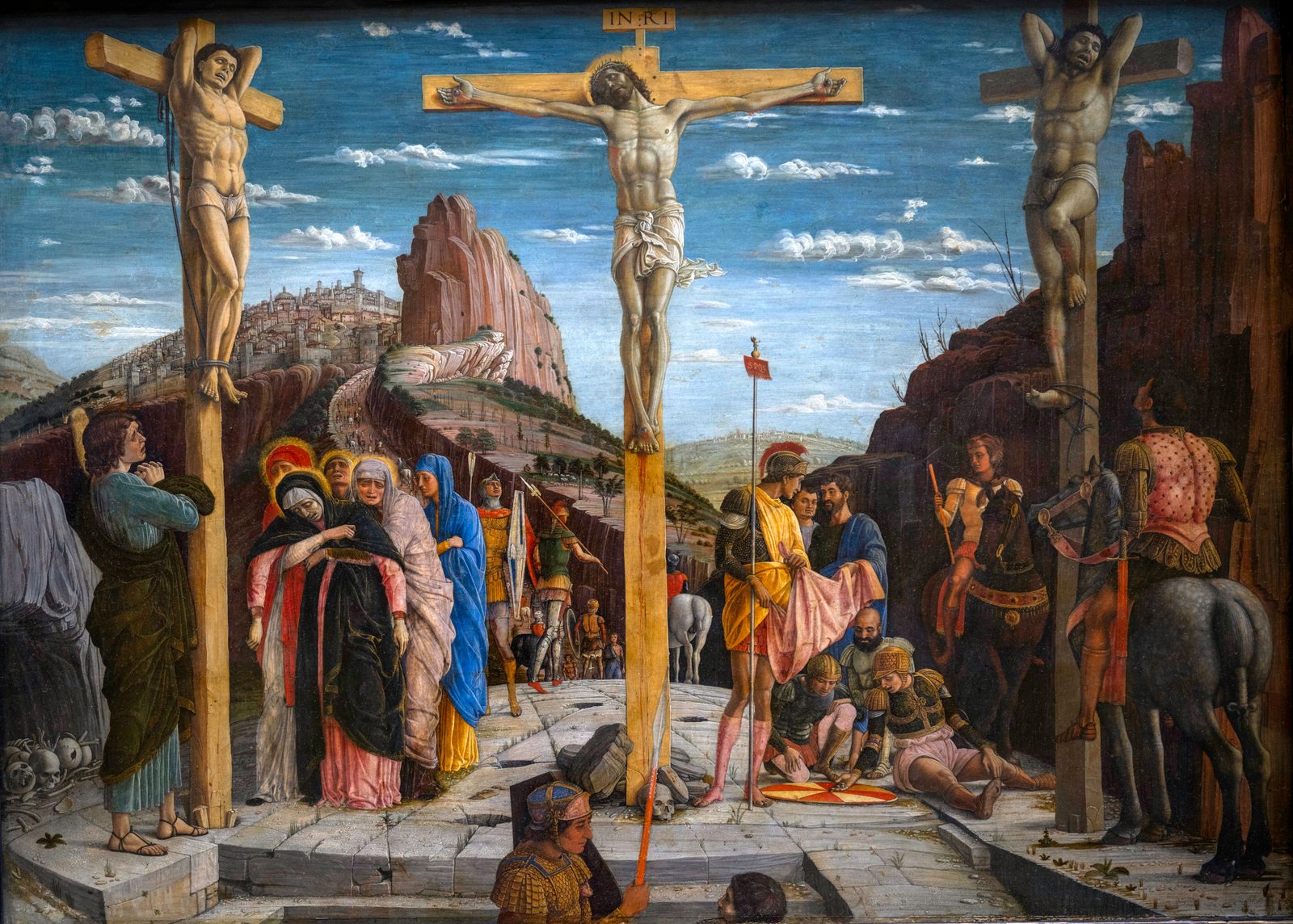 Three crosses on a stone hill above a walled city; at the left women hold Mary as she sinks, and at the right soldiers cast lots for a robe on a round shield.