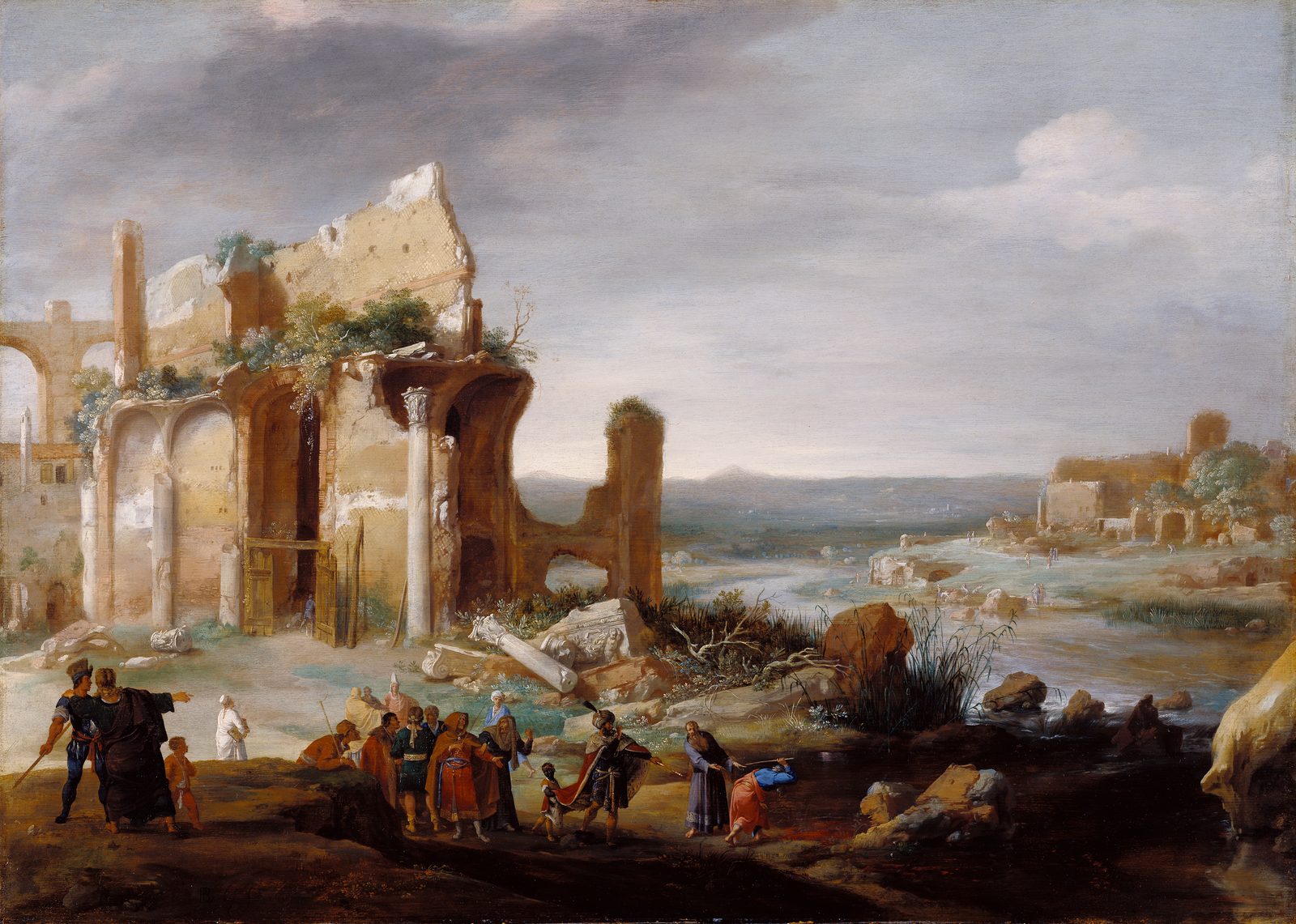 Beside tall ruins on a riverbank, a robed man bends to touch the water with a staff while a crowd in bright robes and turbans watches, and the river runs off into a wide valley.